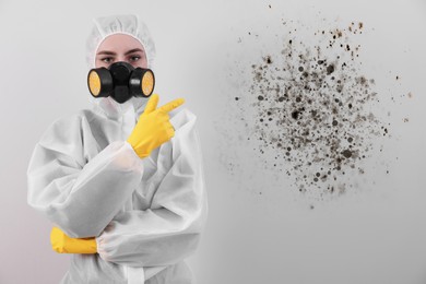 Woman in protective suit pointing at wall affected with mold