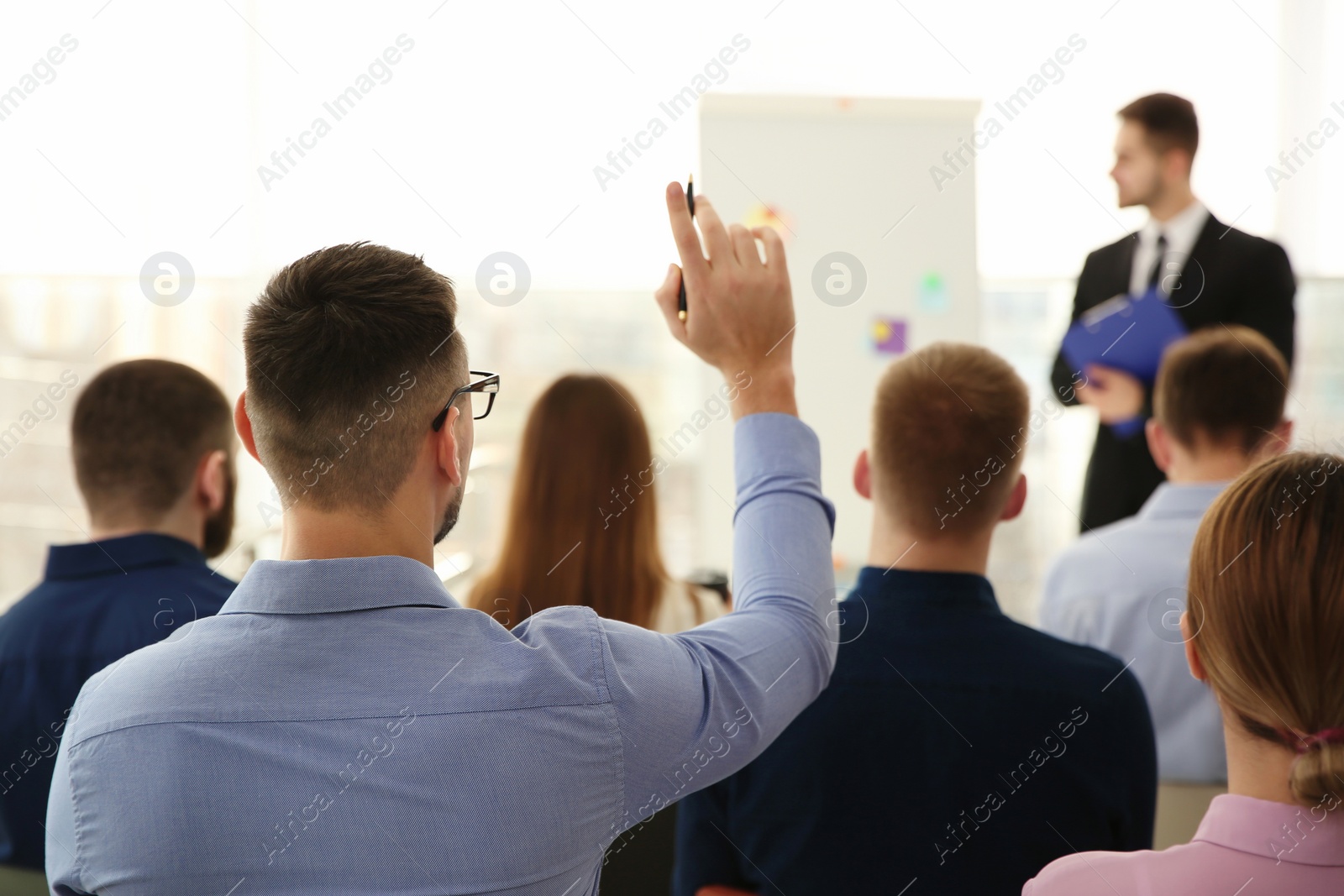 Photo of Man raising hand to ask question at business training indoors, back view