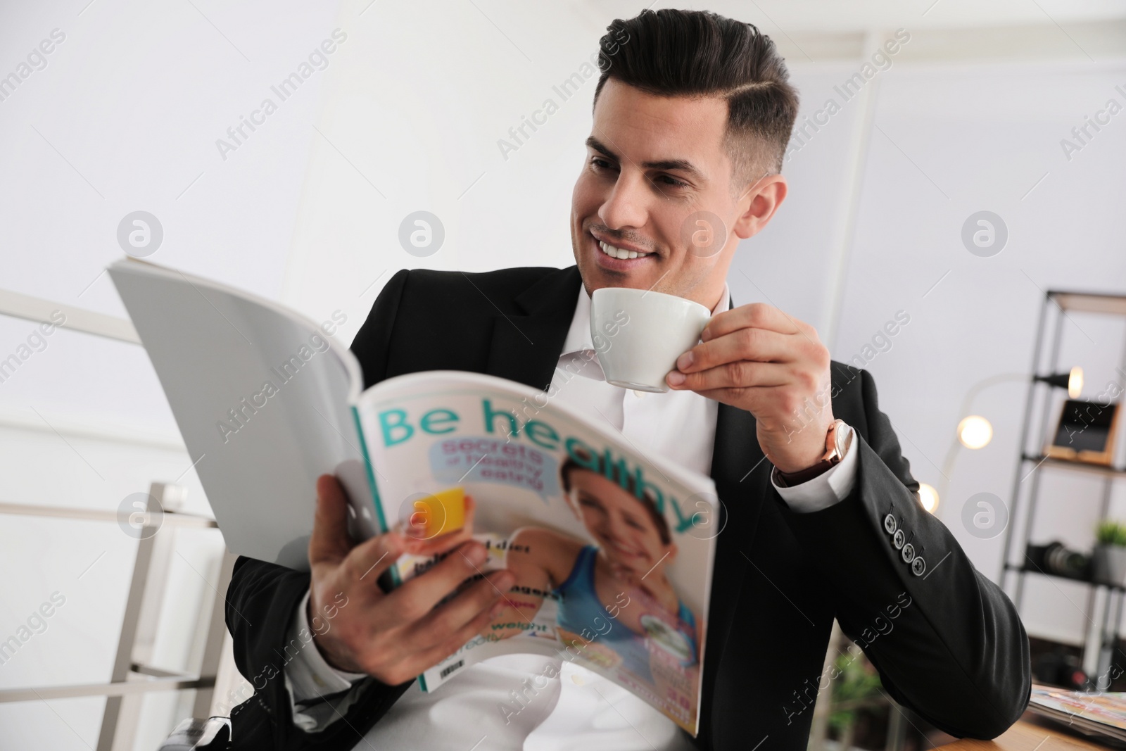 Photo of Man with cup reading magazine at table in office