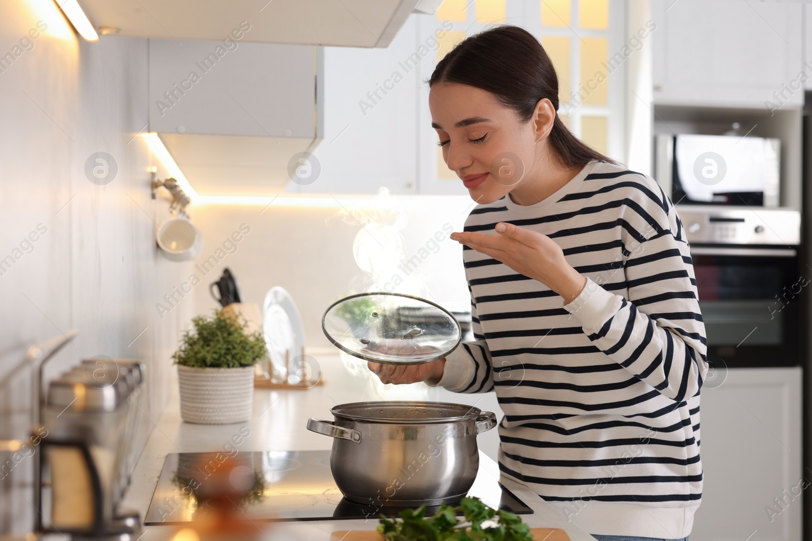 Photo of Beautiful woman smelling aromatic soup in kitchen