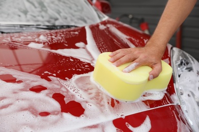 Man washing red auto with sponge at car wash, closeup