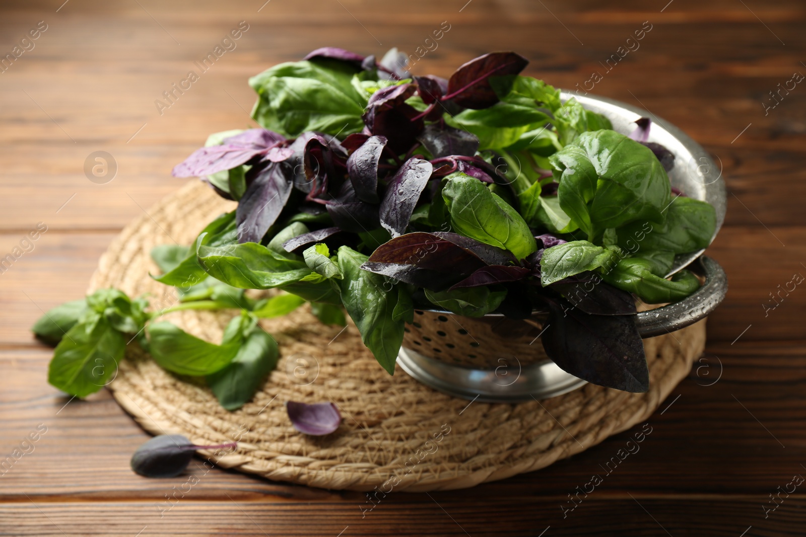 Photo of Metal colander with different fresh basil leaves on wooden table, closeup