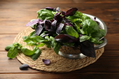 Photo of Metal colander with different fresh basil leaves on wooden table, closeup