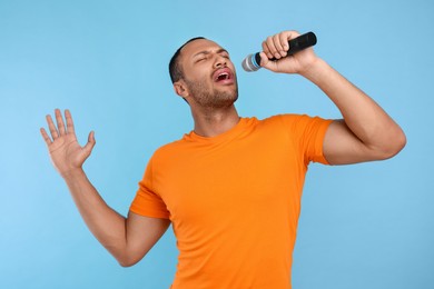 Handsome man with microphone singing on light blue background