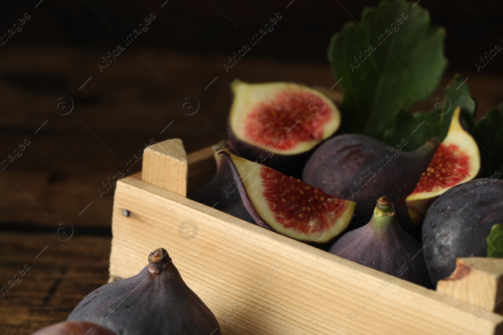 Photo of Whole and cut tasty fresh figs in wooden crate, closeup