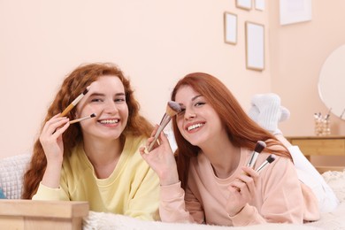 Photo of Portraitbeautiful young redhead sisters with makeup brushes at home