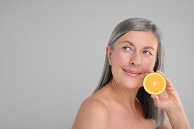 Photo of Beautiful woman with half of orange rich in vitamin C on grey background, space for text