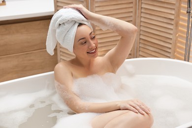 Photo of Happy woman taking bath with foam in tub indoors
