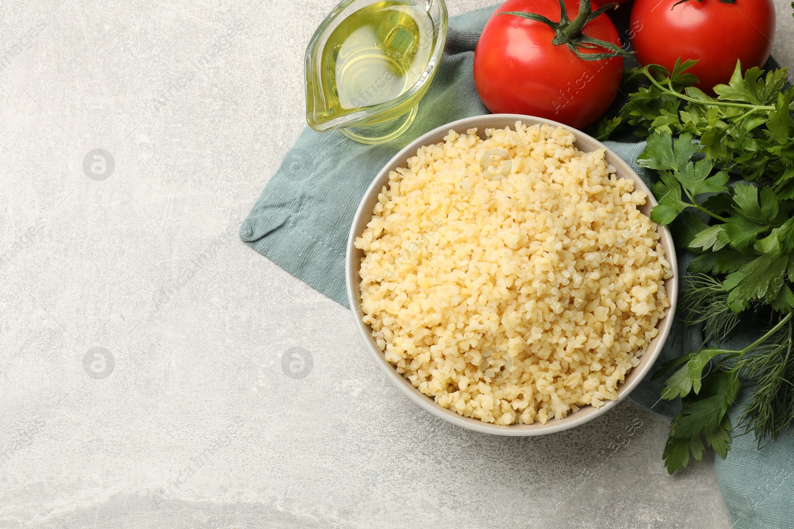 Photo of Delicious bulgur in bowl, tomatoes, greens and oil on gray table, top view. Space for text