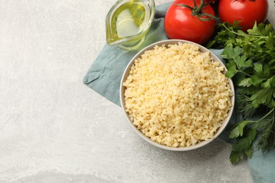 Delicious bulgur in bowl, tomatoes, greens and oil on gray table, top view. Space for text