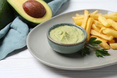 Photo of Plate with french fries, guacamole dip, parsley and avocado served on white wooden table, closeup