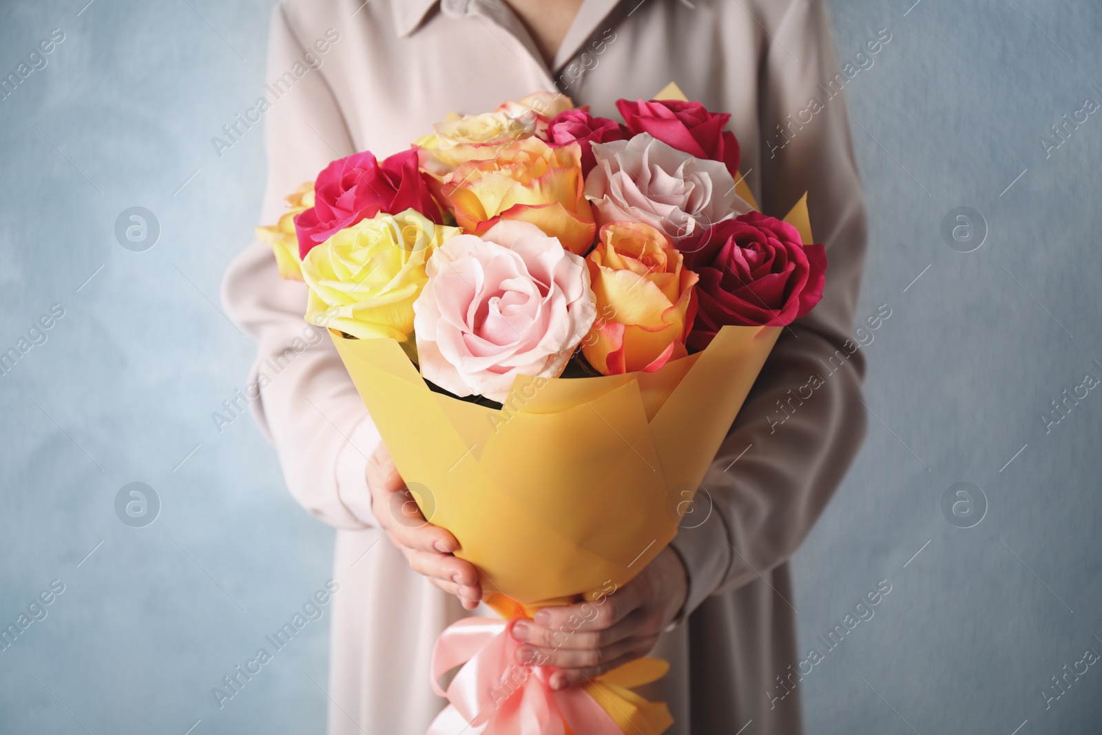 Photo of Woman holding luxury bouquet of fresh roses on light blue background, closeup