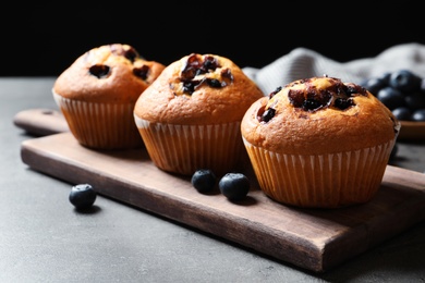 Photo of Wooden board with blueberry muffins on grey table against black background, closeup view