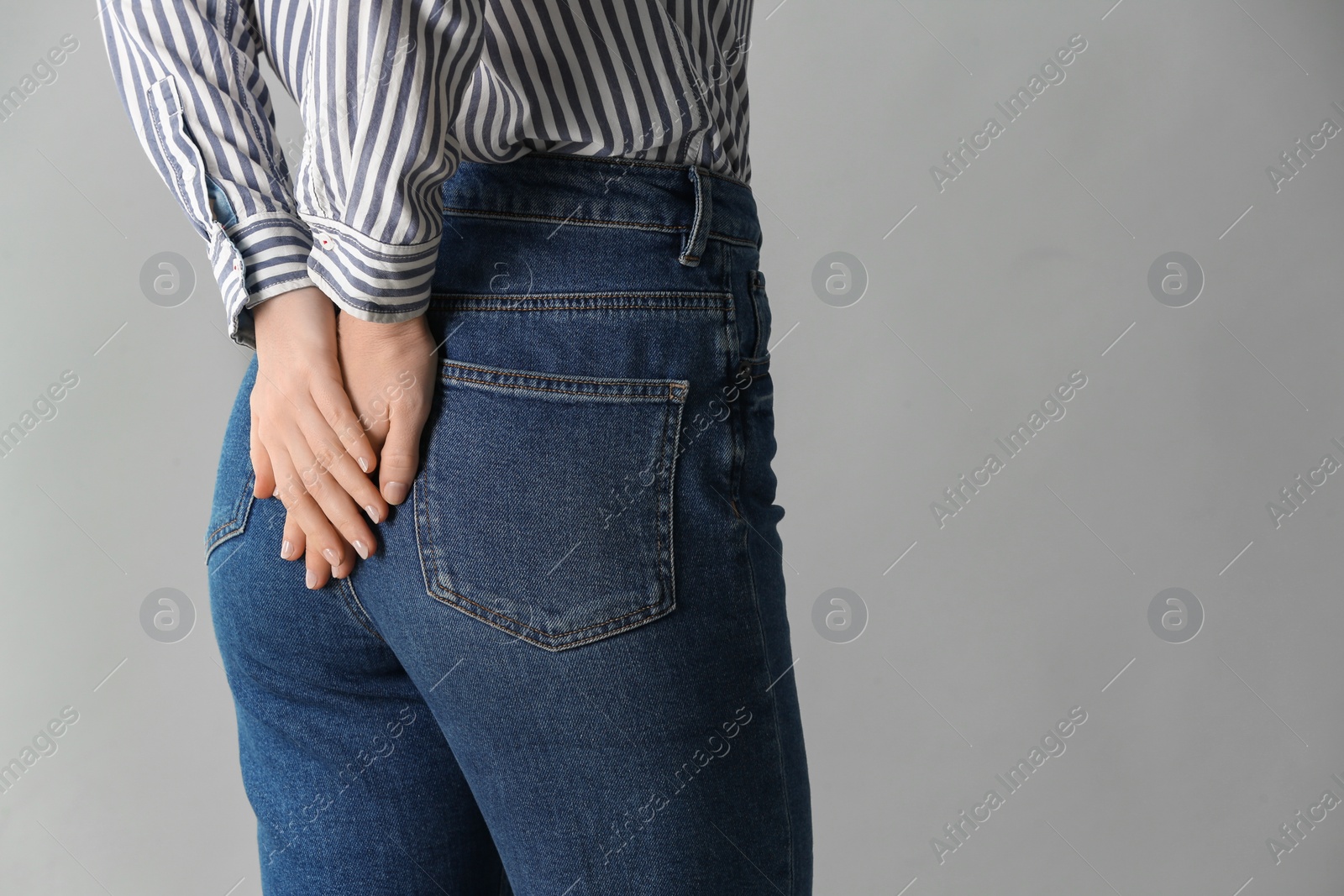 Photo of Woman suffering from hemorrhoid on light grey background, closeup. Space for text