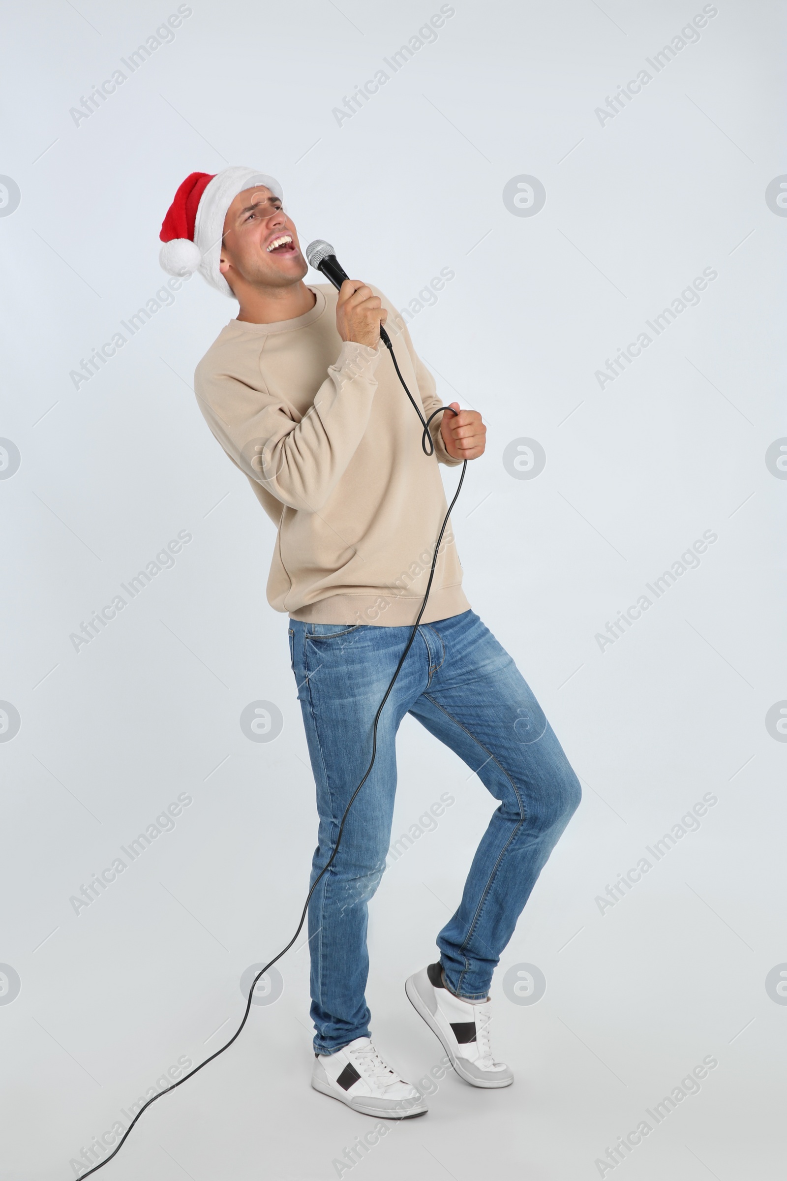 Photo of Emotional man in Santa Claus hat singing with microphone on white background. Christmas music