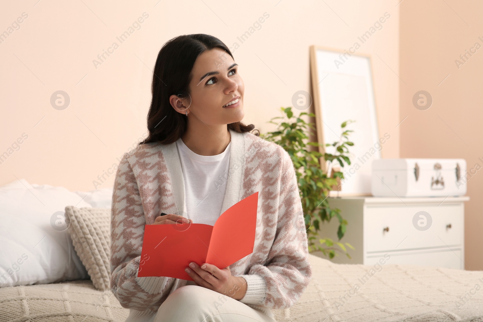 Photo of Young woman writing message in greeting card indoors, space for text