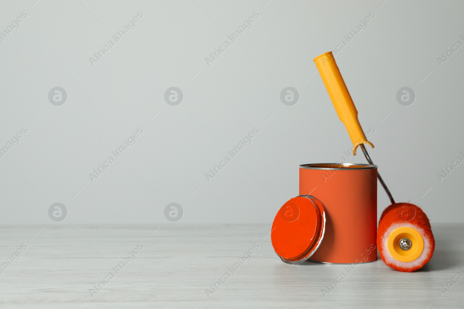 Photo of Can of orange paint and roller on white wooden table. Space for text