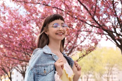 Photo of Beautiful young woman in park with blossoming sakura trees