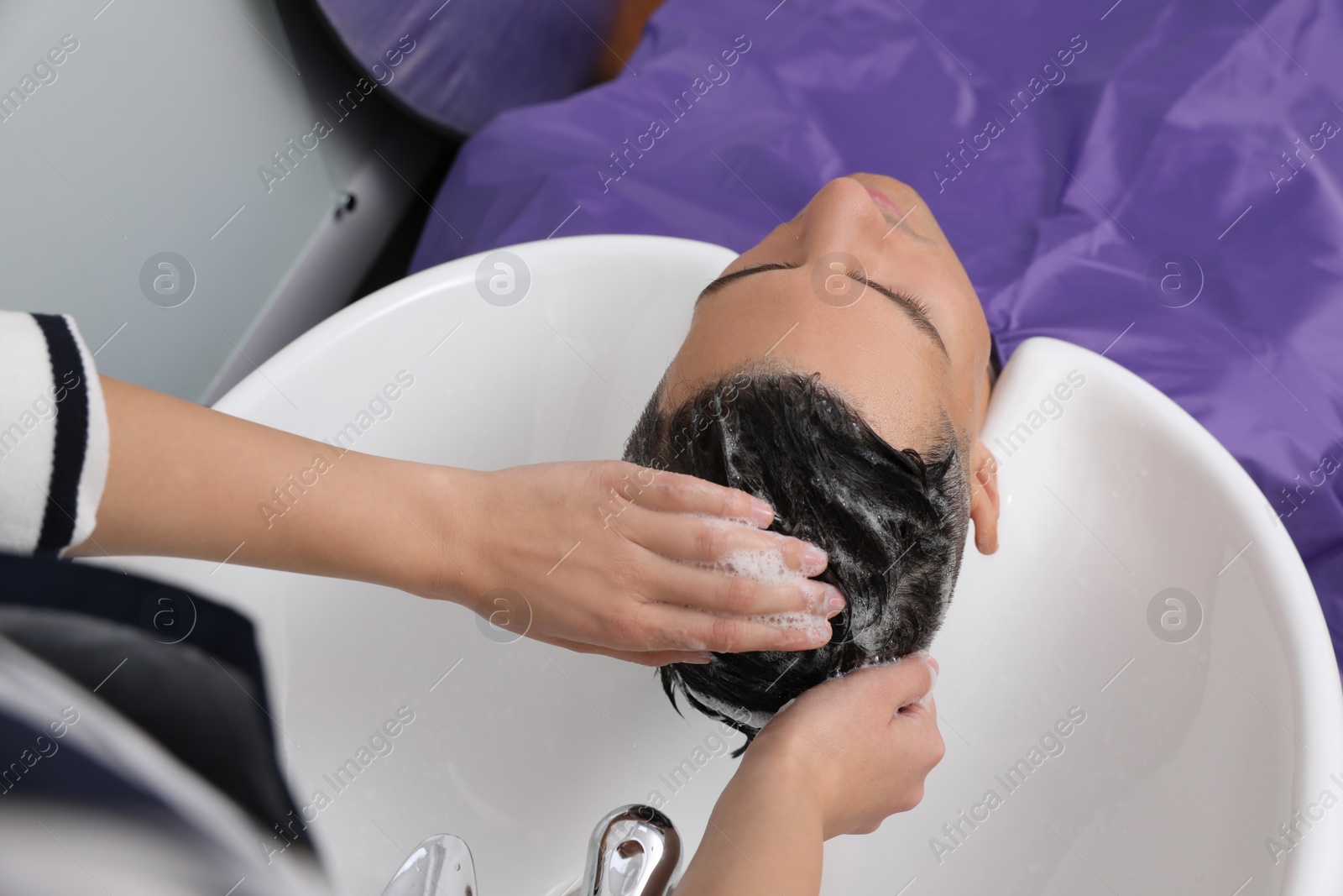 Photo of Professional hairdresser washing client's hair at sink in salon, above view