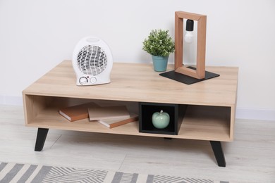 Photo of Electric fan heater and different decor elements on wooden coffee table at home