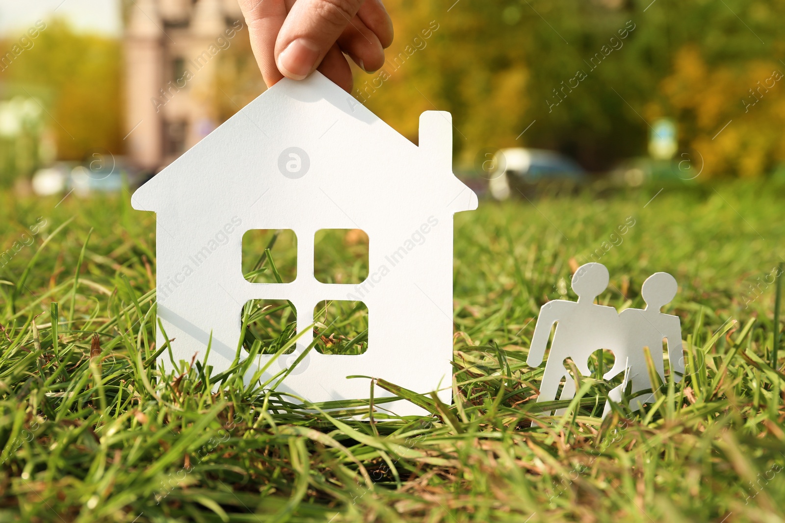 Photo of Woman with paper silhouettes of house and family in grass outdoors. Life insurance concept