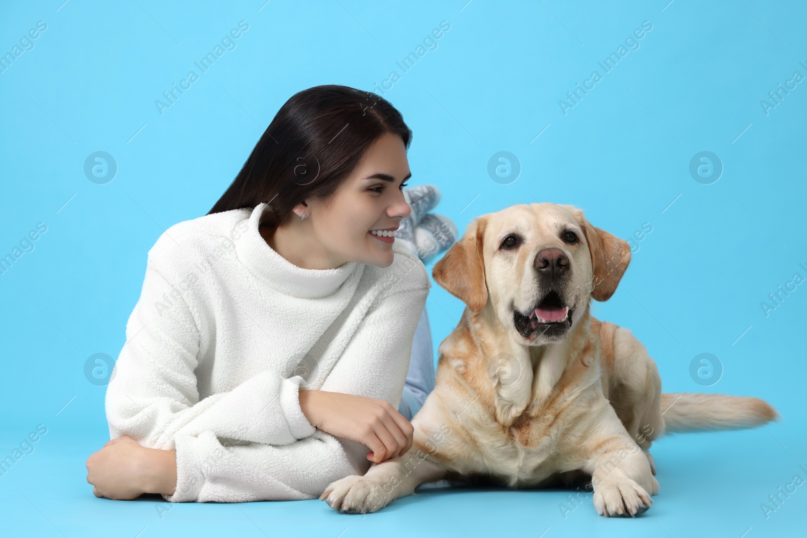 Photo of Happy woman with cute Labrador Retriever on light blue background