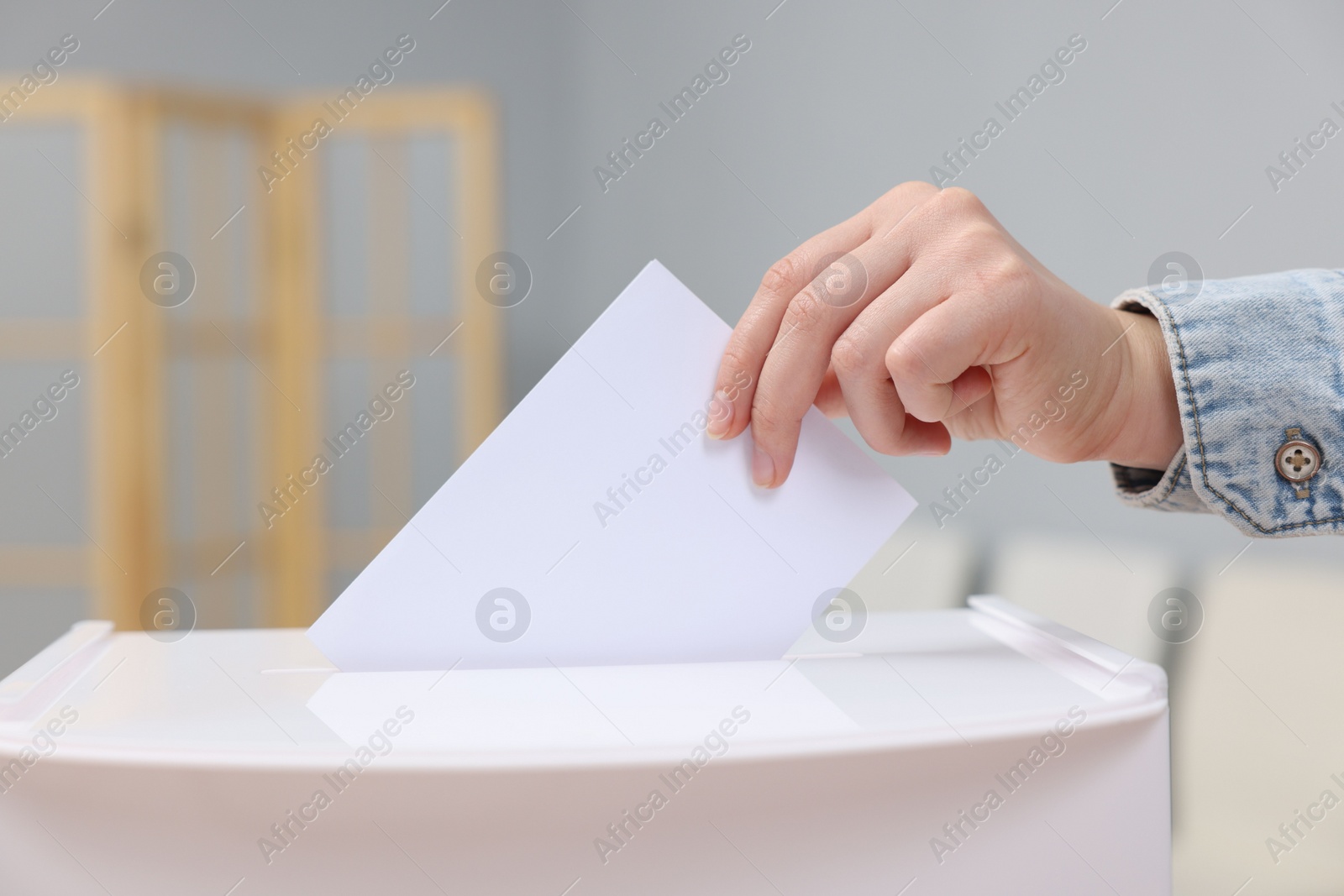 Photo of Woman putting her vote into ballot box on blurred background, closeup