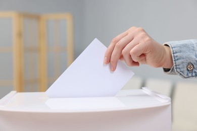 Photo of Woman putting her vote into ballot box on blurred background, closeup