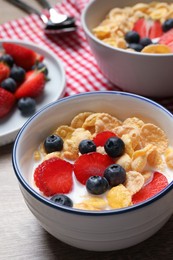 Photo of Delicious crispy cornflakes with milk and fresh berries on wooden table, closeup