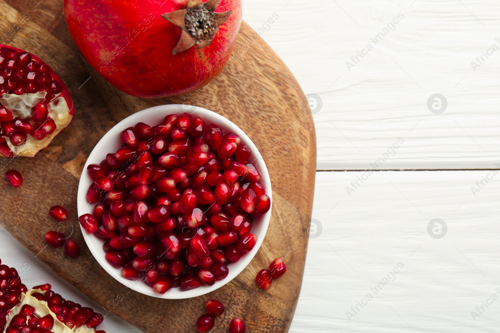 Photo of Ripe juicy pomegranate grains on white wooden table, top view. Space for text