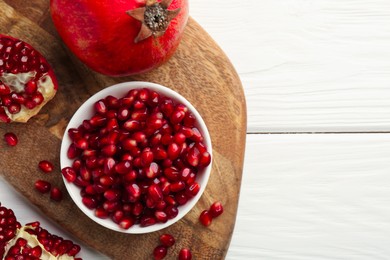 Photo of Ripe juicy pomegranate grains on white wooden table, top view. Space for text