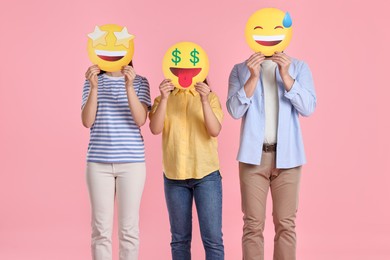 People covering faces with emoticons on pink background