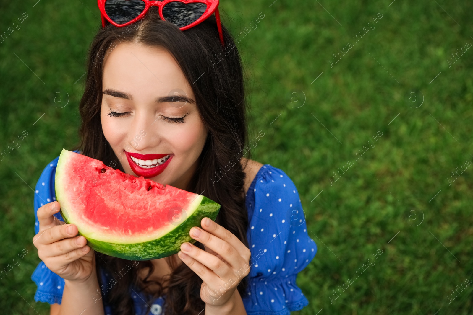 Photo of Beautiful young woman with watermelon on green grass outdoors. Space for text