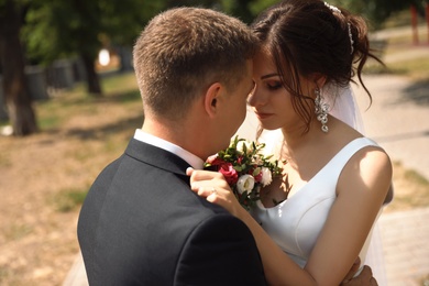 Happy newlyweds with beautiful bridal bouquet outdoors