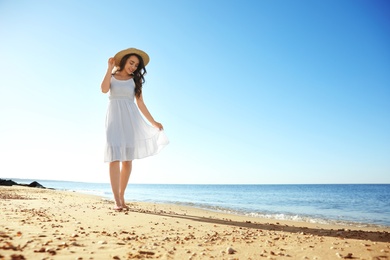 Photo of Happy young woman with hat walking on beach near sea. Space for text