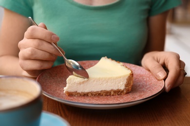 Photo of Woman eating slice of cheesecake at table, closeup