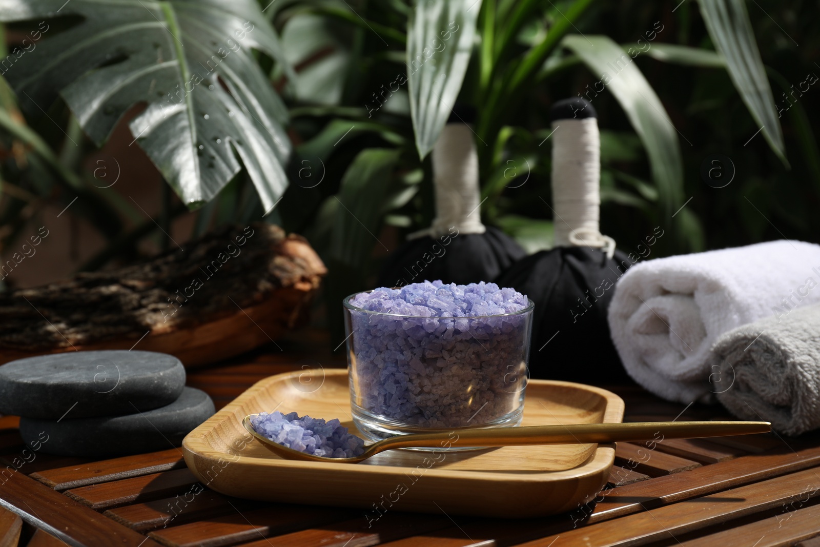 Photo of Bowl of purple sea salt, spoon and rolled towels on wooden table