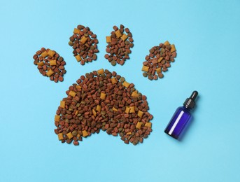 Photo of Tincture in glass bottle near pet footprint of pelleted dry food on light blue background, flat lay