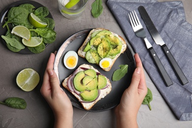 Photo of Woman with tasty avocado toasts over grey table, top view