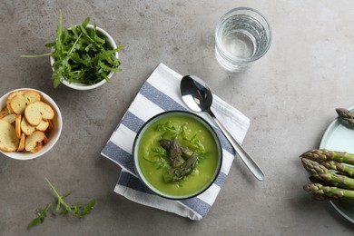 Delicious asparagus soup served on grey table, flat lay