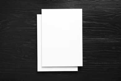 Photo of Stack of blank paper sheets for brochure on black wooden background, top view. Mock up