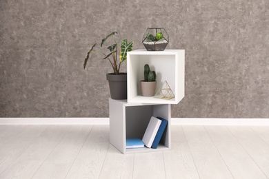 Shelving unit with indoor plants and books for interior design on floor at grey wall. Trendy home decor