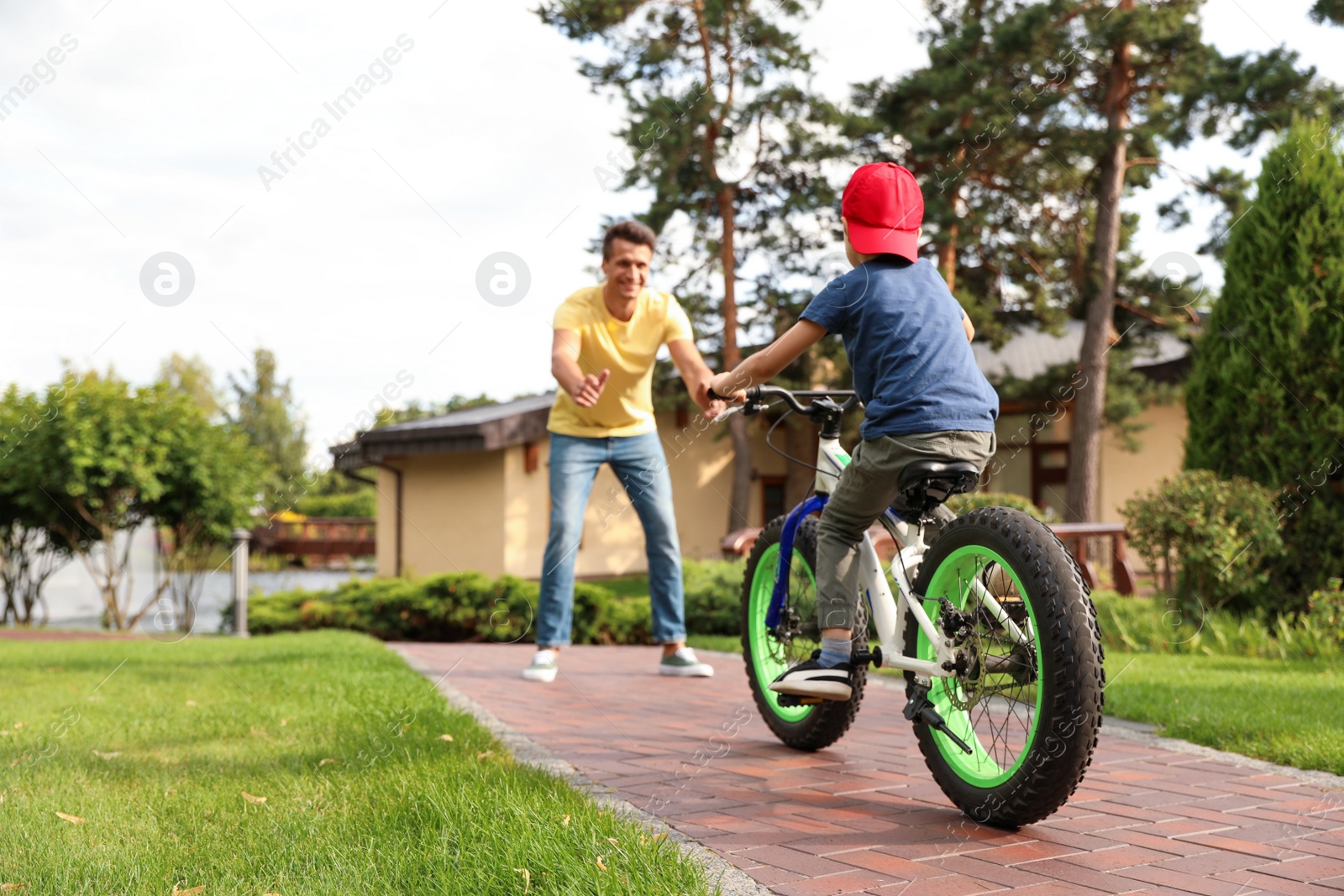 Photo of Dad teaching son to ride bicycle outdoors