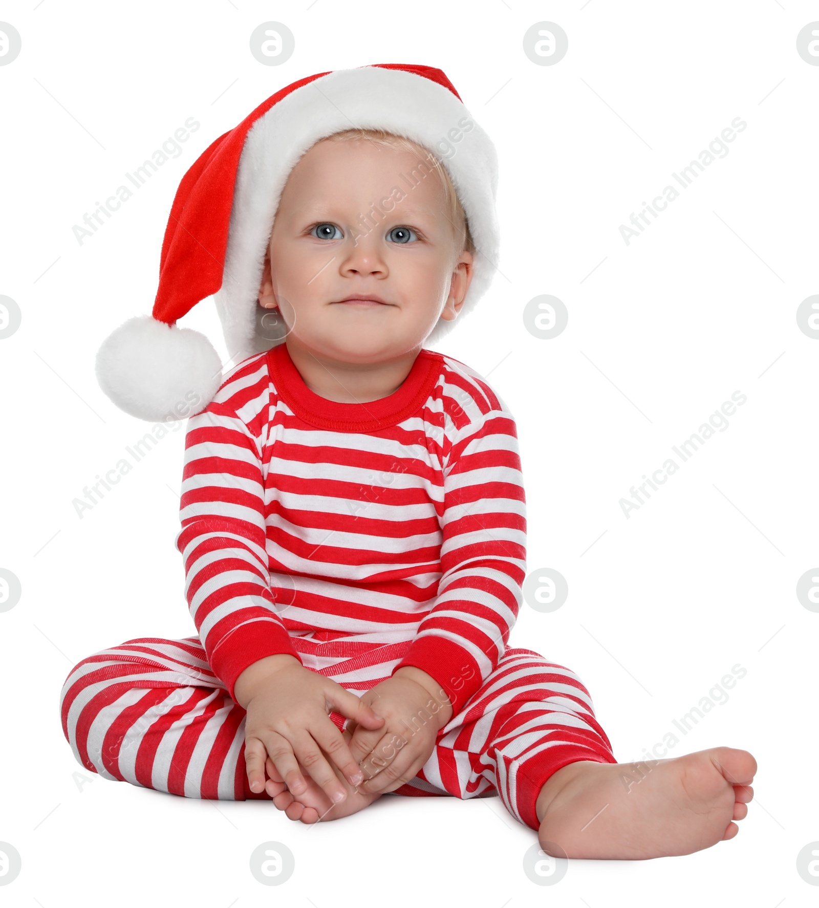 Photo of Cute baby in Santa hat and Christmas pajamas sitting on white background