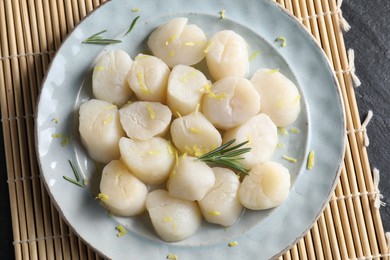 Photo of Raw scallops with lemon and rosemary on dark textured table, top view