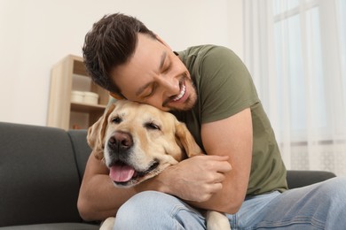 Photo of Man hugging his cute Labrador Retriever on sofa at home