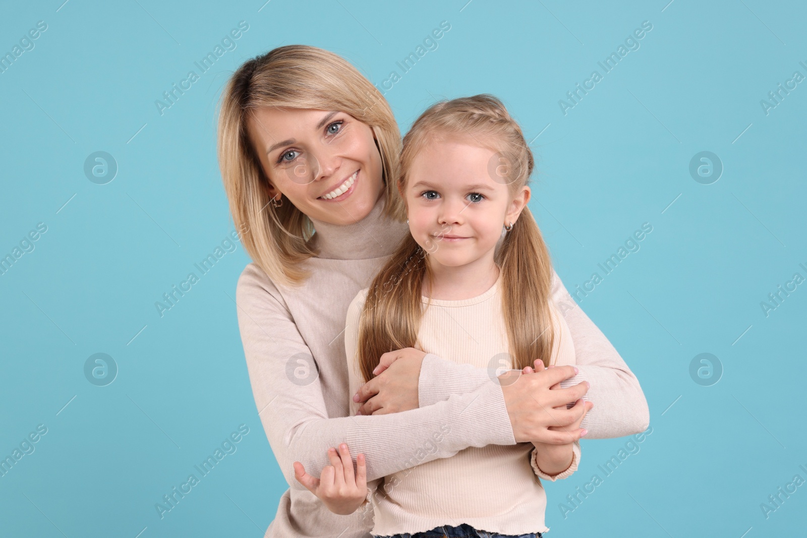 Photo of Mother hugging her happy daughter on light blue background