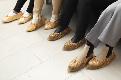 Women wearing shoe covers onto different footwear indoors, closeup