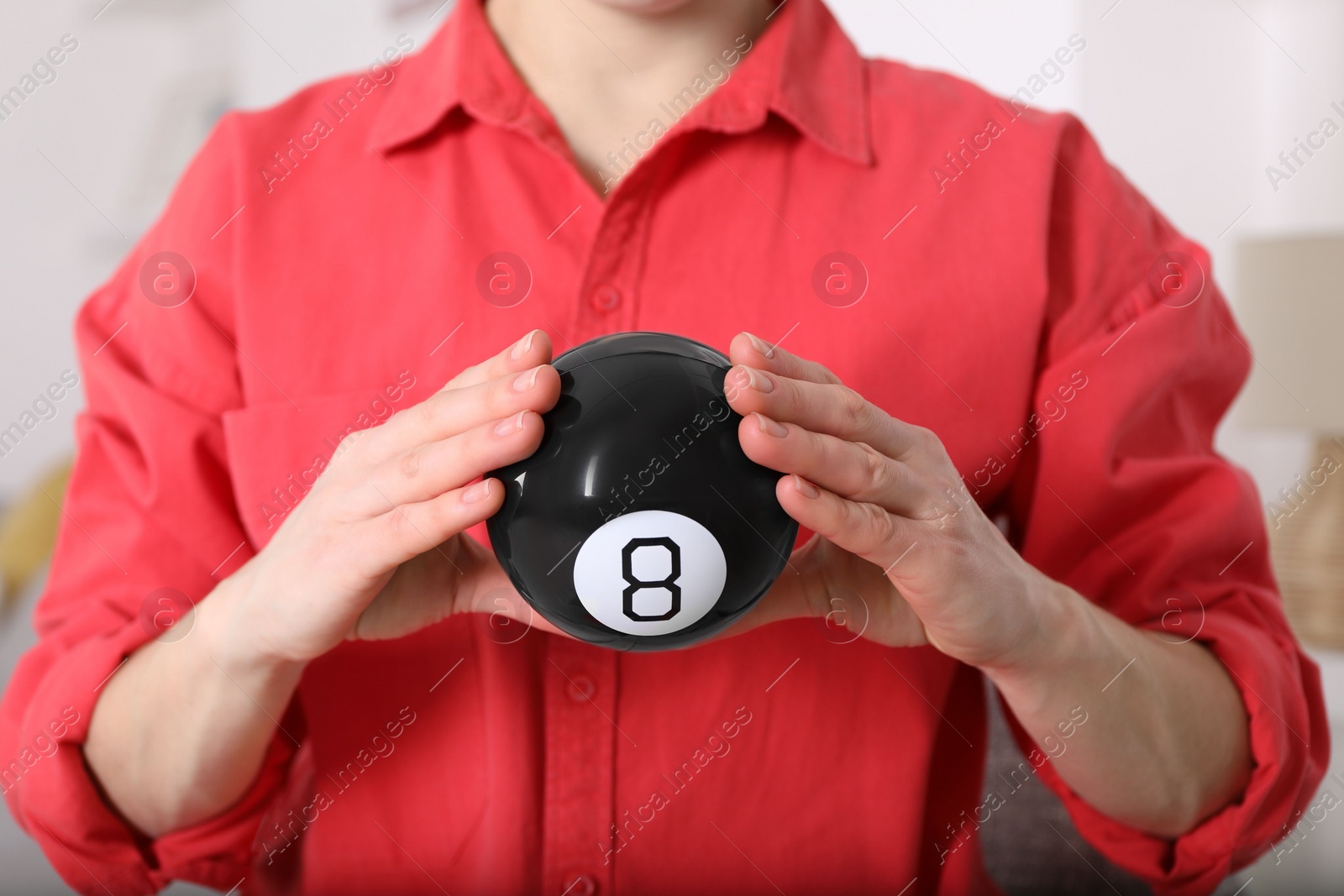 Photo of Woman holding magic eight ball indoors, closeup