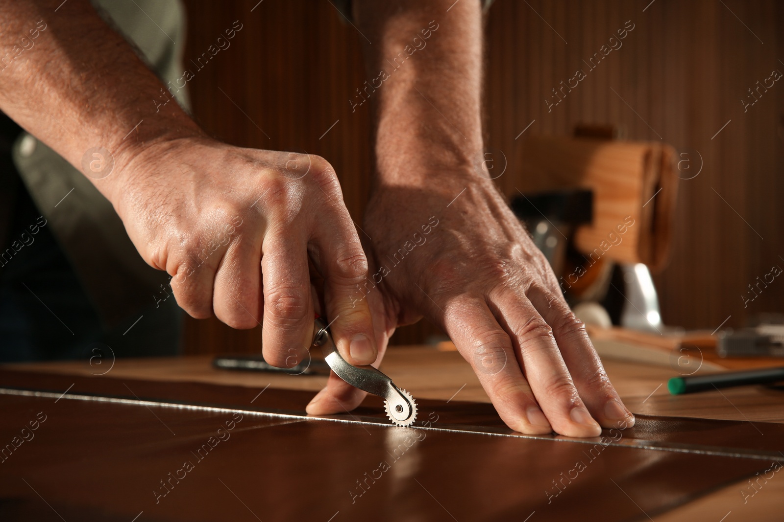 Photo of Man marking leather with roller in workshop, closeup